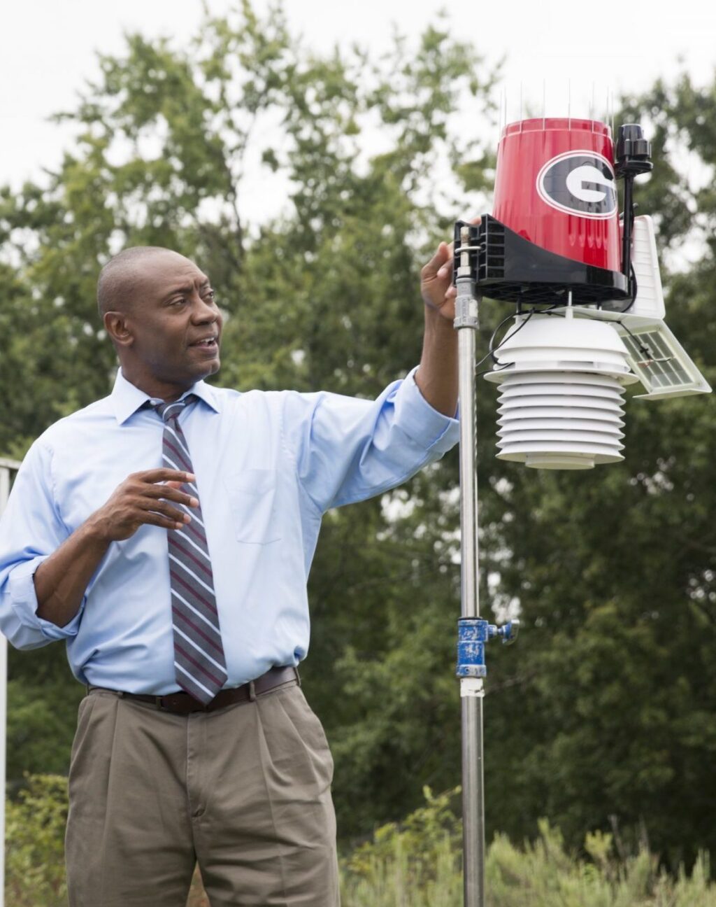 J. Marshall Shepherd standing in a field holding a weather device with the UGA logo.