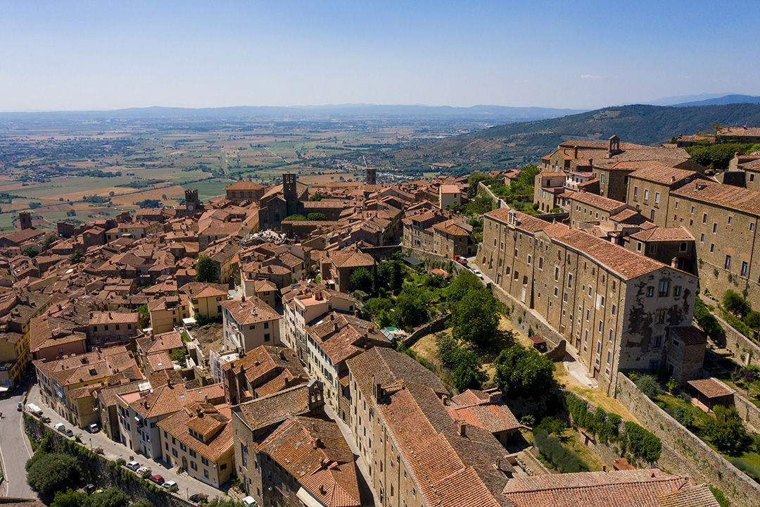 Aerial image of the city of Cortona, Italy, with the Chiana Valley and the Tuscany countryside in the background.