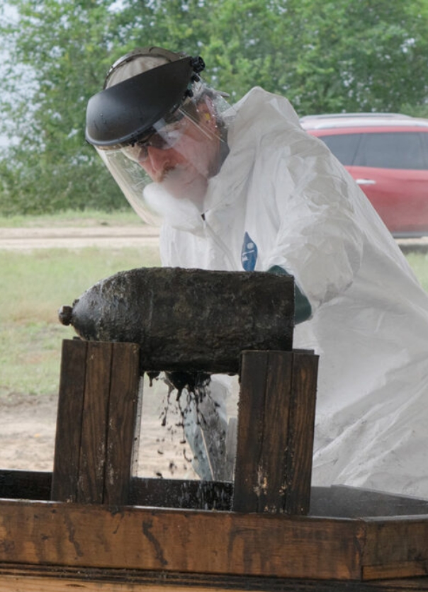 Man wearing a protective suit and mask and spraying a liquid on an explosive device